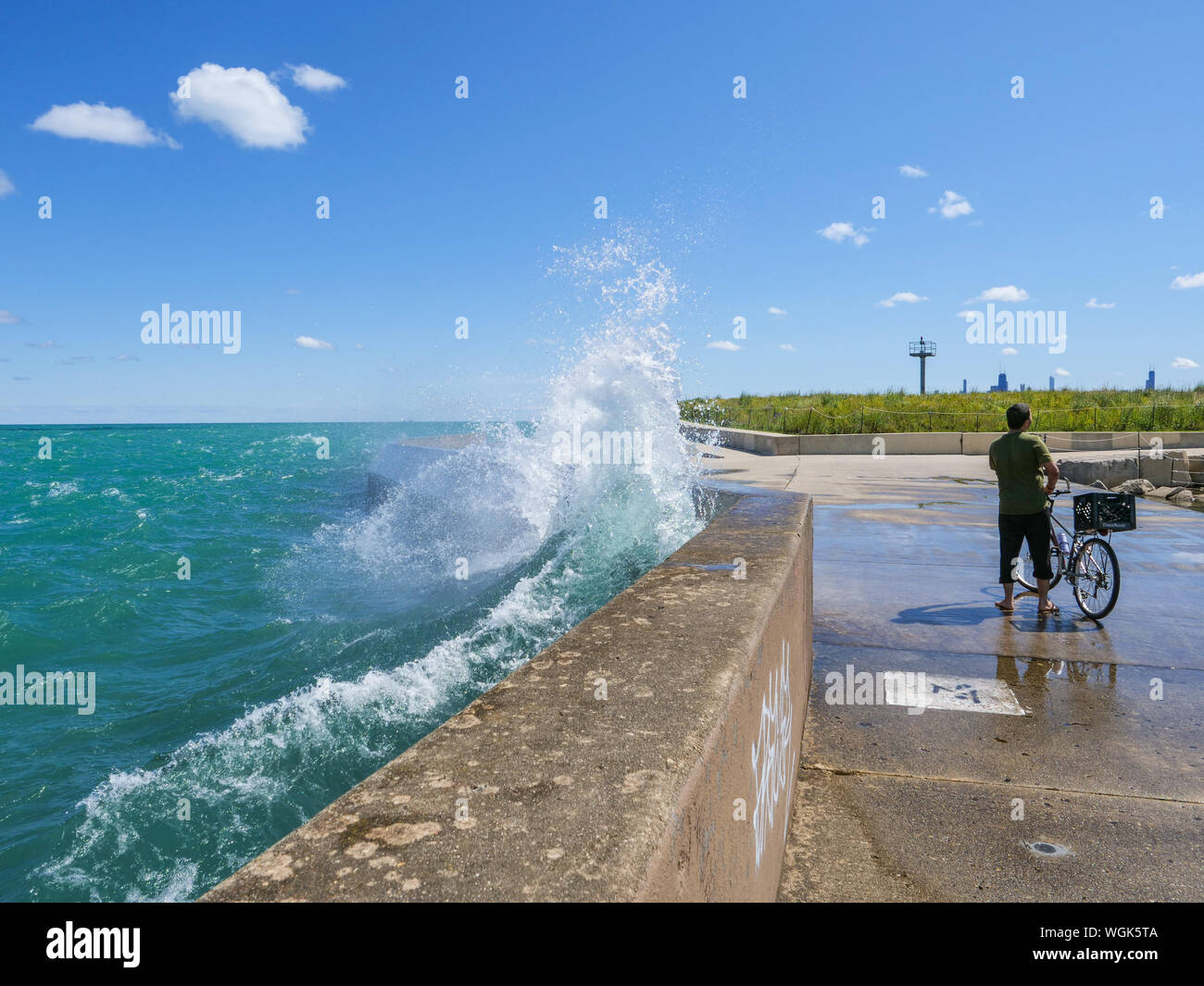 Una grande onda plätscherten seawall dietro un ciclista a Montrose punto, Chicago, Illinois. Foto Stock