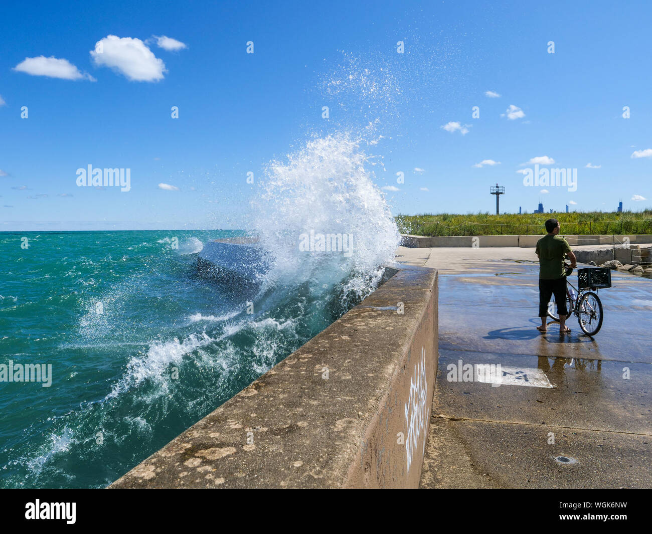 Una grande onda plätscherten seawall dietro un ciclista a Montrose punto, Chicago, Illinois. Foto Stock
