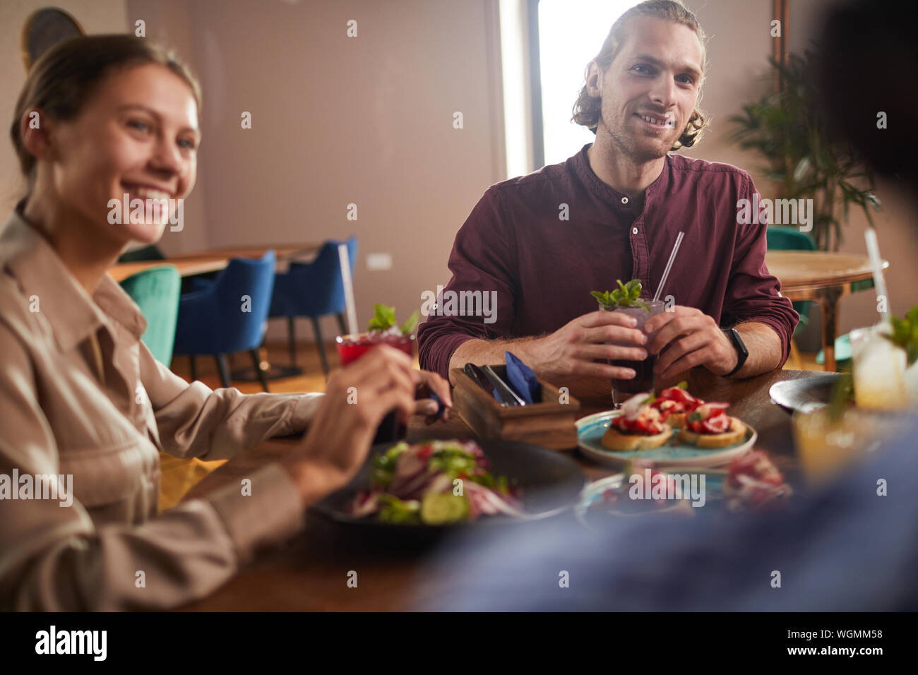 Gruppo di amici gustando un pranzo insieme seduta a tavola in cafe, focus sul bel giovane, spazio di copia Foto Stock