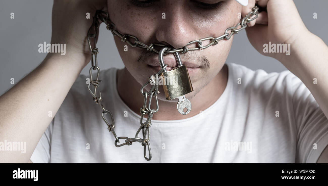 Teen bocca coperto da rusty catena e lucchetto a lui proibita la libera speeching. Isolato su sfondo grigio Foto Stock
