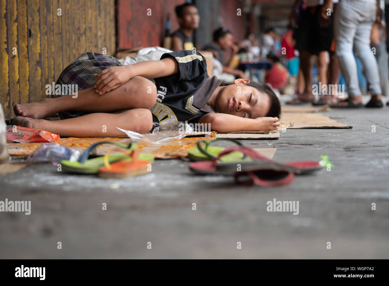 Un giovane ragazzo di dormire su un marciapiede utilizzando cartone come biancheria da letto Foto Stock