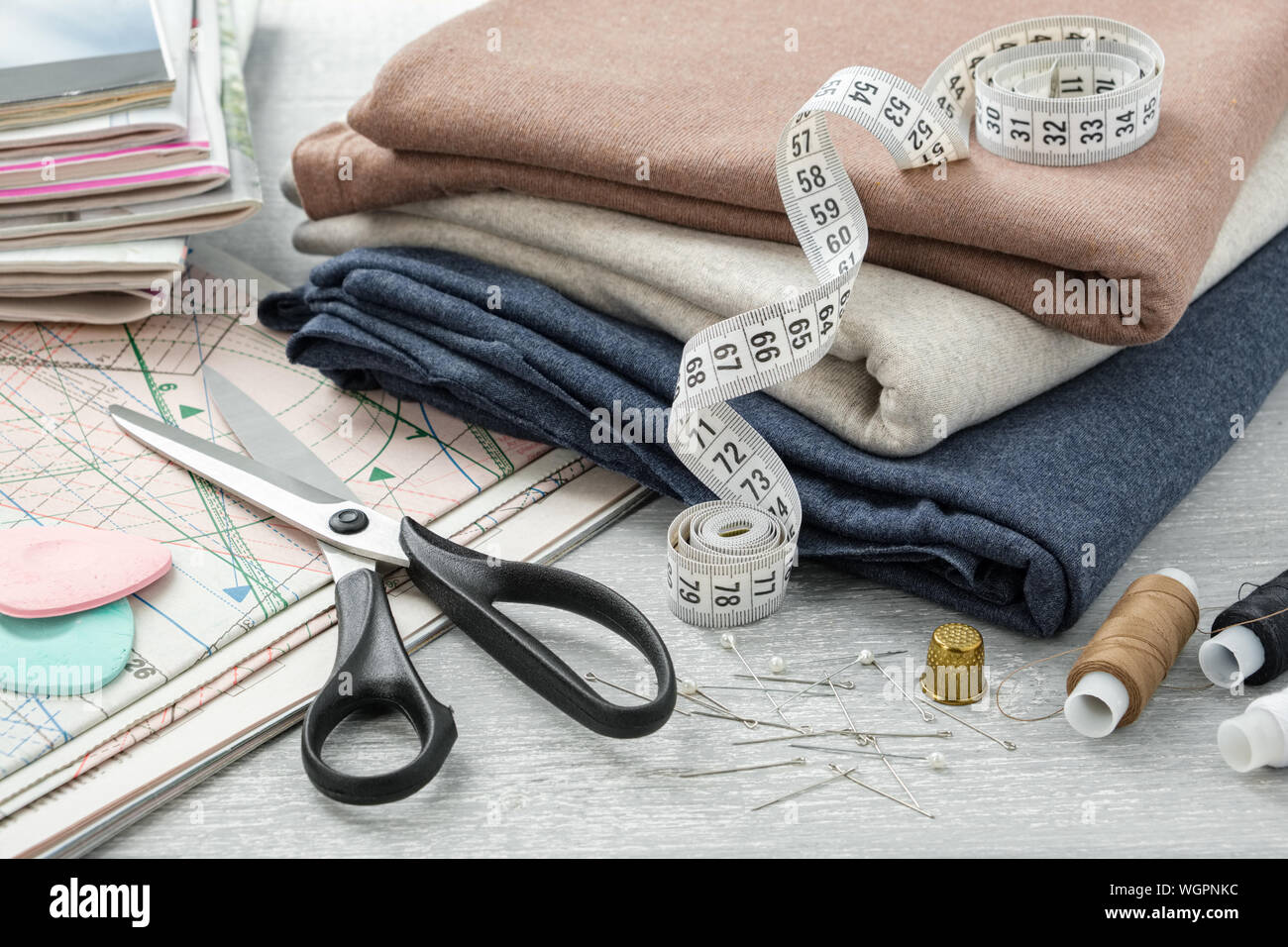 Elementi di cucitura: tessuti colorati, forbici, nastro di misurazione, ditale, rocchetti di fili, compresi i pin, i gessi, modello di cucitura e riviste su una tavoletta grafica Foto Stock