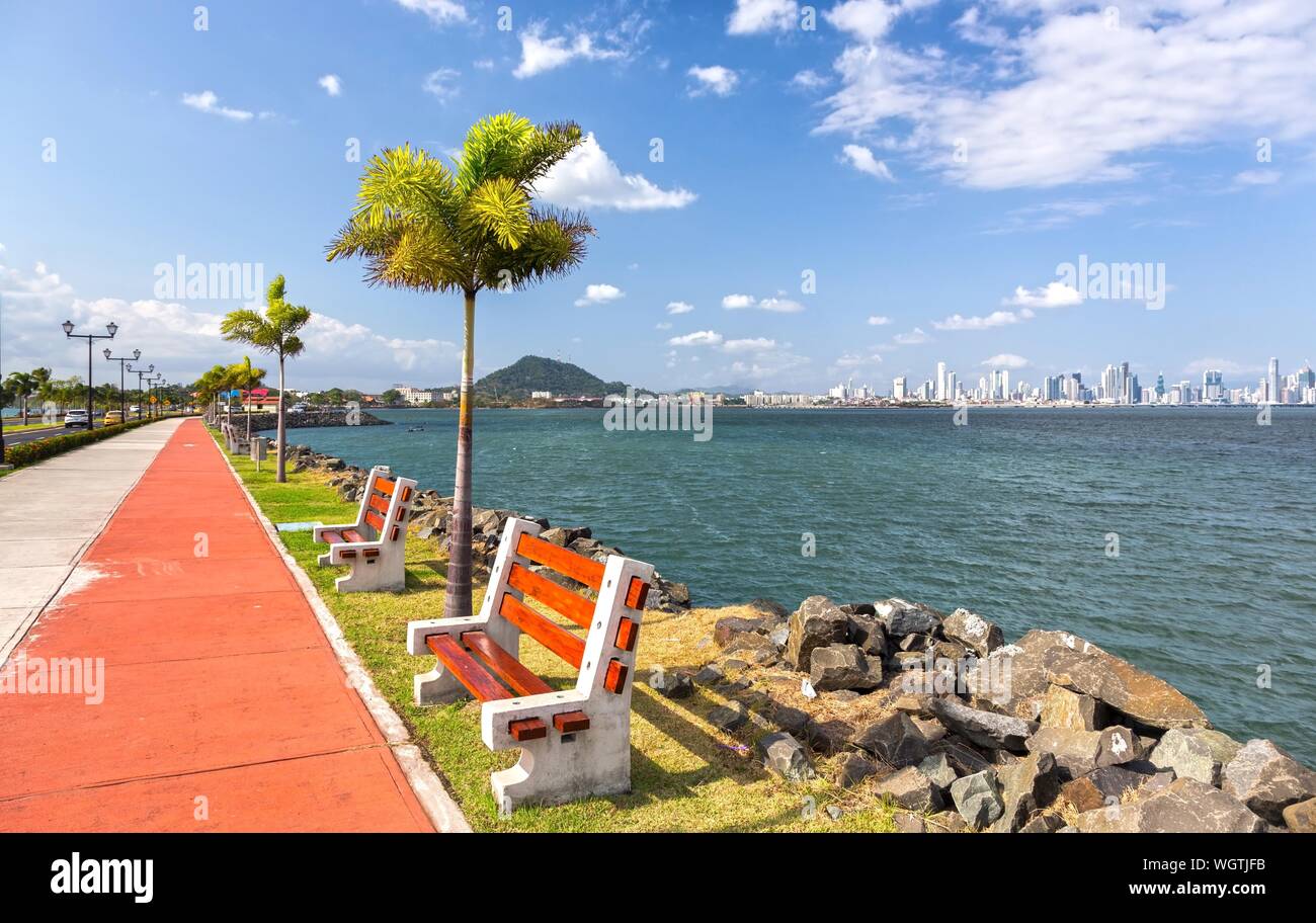 Il Amador Causeway Road, Panama City famoso boom Boardwalk e di attrazione turistica con panchine, palme e centro città skyline sull orizzonte Foto Stock