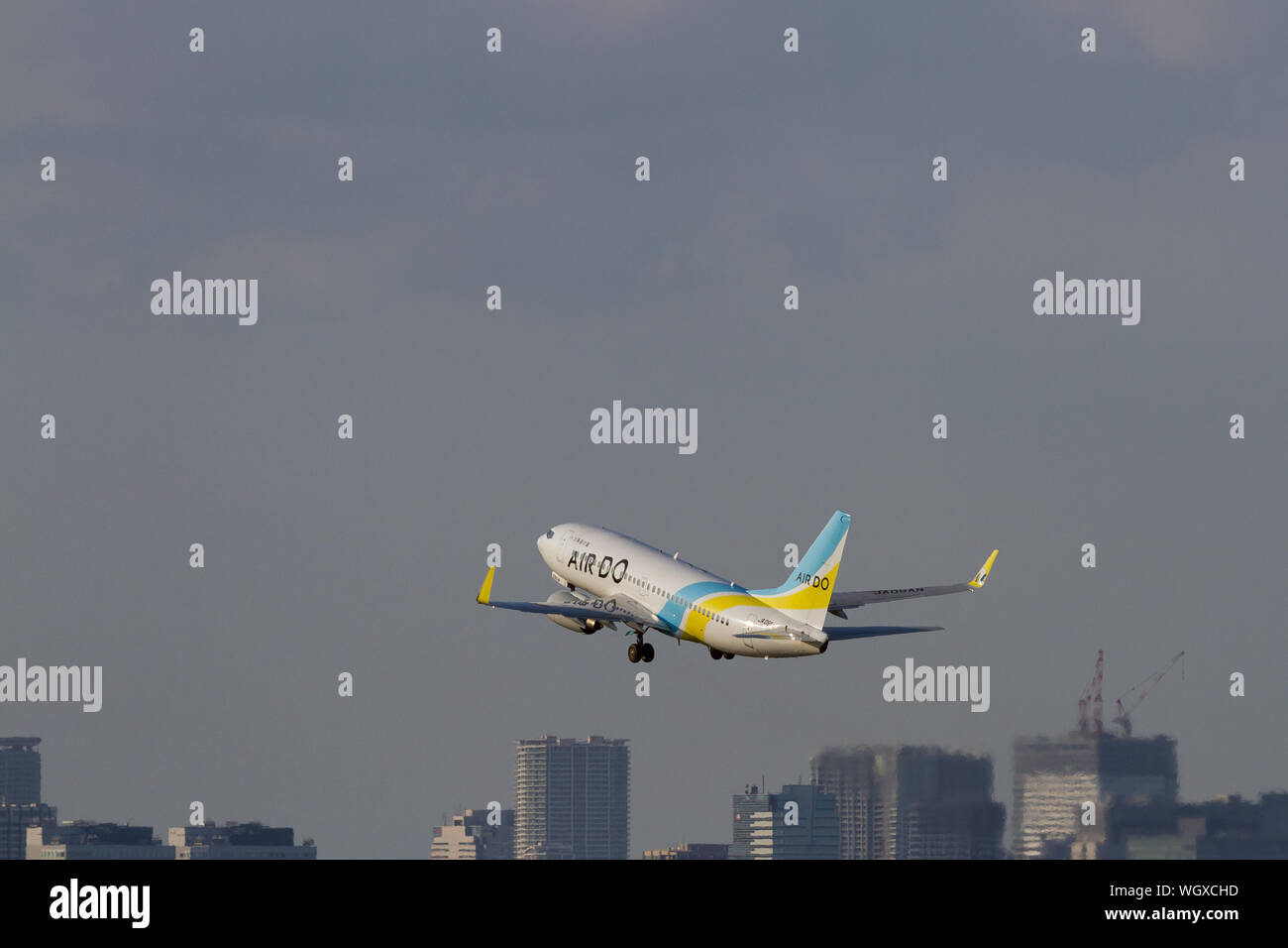 Un Boeing 737-781, gestito da una compagnia aerea di bilancio, Air Do, decolla dall'aeroporto di Haneda, di fronte agli edifici di Tokyo, Giappone. Foto Stock