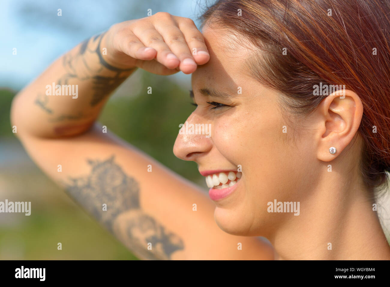 Attraente donna sorridente mantenendo un look out con la sua mano alzata a sua fronte per schermare gli occhi dal sole e un sorriso Foto Stock