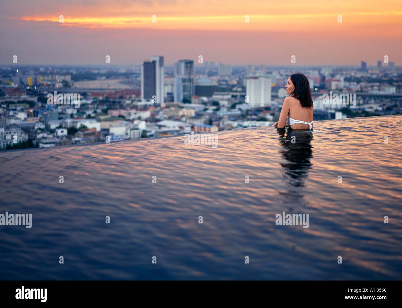 Giovane donna rilassarsi nella piscina sul tetto durante un tramonto meraviglioso e godetevi la vista della citta'. Vacanze estive e vacanze concept Foto Stock