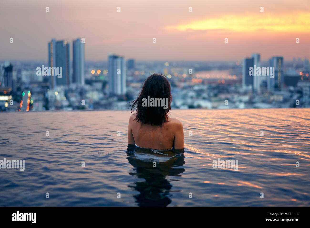 Giovane donna rilassarsi nella piscina sul tetto durante un tramonto meraviglioso e godere la città. Vacanze estive e vacanze concept Foto Stock
