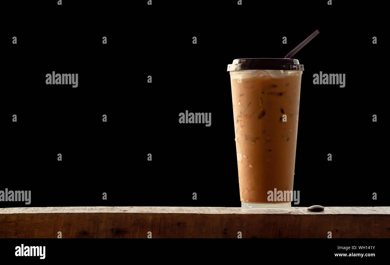 Caffè ghiacciato in un bicchiere di plastica su legno , sfondo nero. Foto Stock