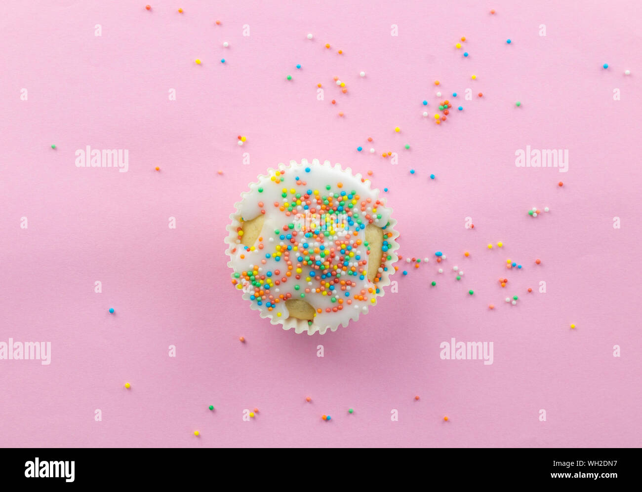 Poco in vetro satinato bianco cupcake nel centro di sfondo rosa cosparso con multi - colorate round spruzza sul Rosa con spazio copia - top viiew foto Foto Stock