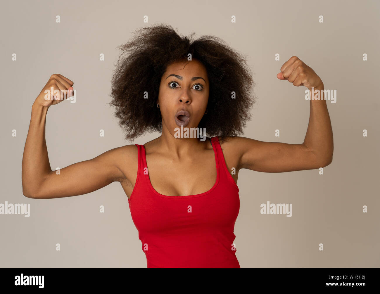 Ritratto di giovane bella funny african american donna con capelli afro style che mostra i muscoli di armi sorridente orgogliosi di divertimento. Nelle persone di successo e Hap Foto Stock