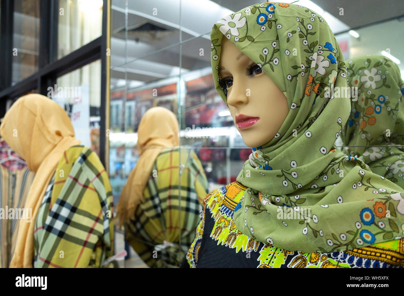 Close up di un manichino con floreale verde hijab musulmano visualizzati contro specchietto esterno negozio di abbigliamento. Foto Stock