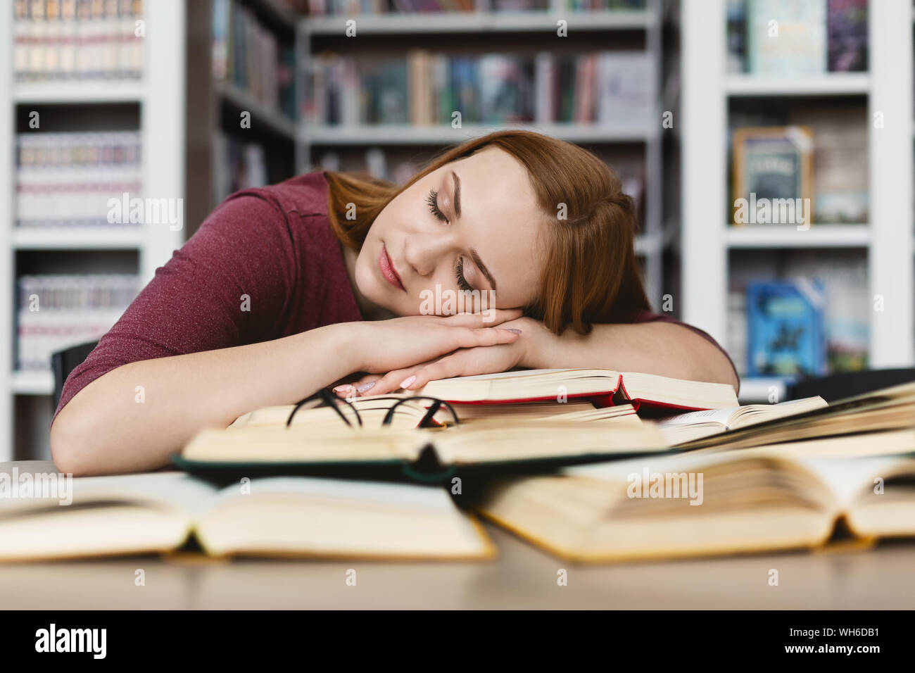 Stanco redhead girl avente nap sui libri in biblioteca Foto Stock