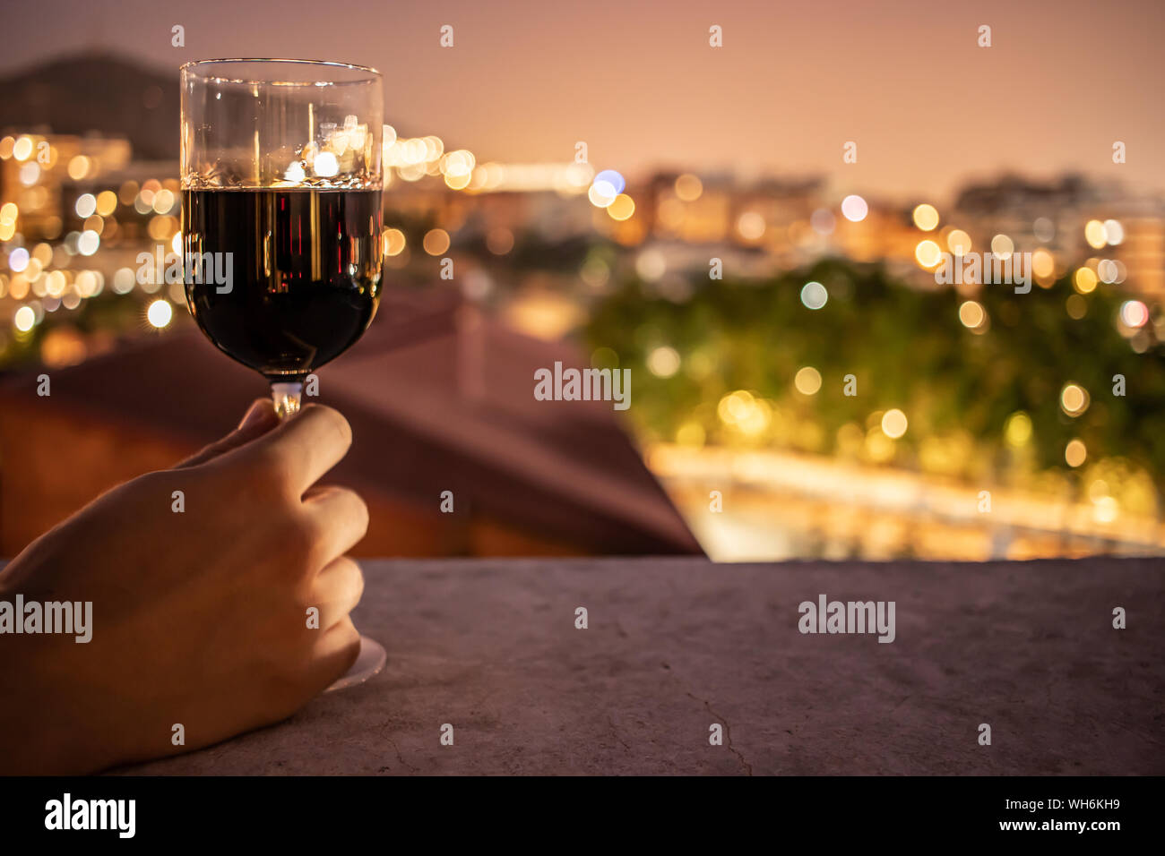 Bicchiere pieno di vino rosso detenute da un maschio di mano davanti a un bellissimo sfocato sullo sfondo della città Foto Stock