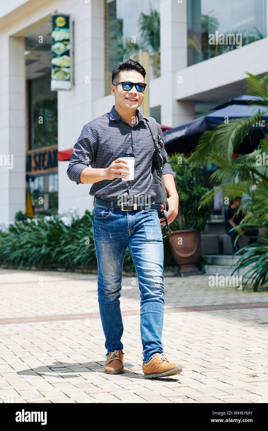 Felice giovane uomo in occhiali da sole passeggiate all'aperto con tazza di caffè sul giorno di estate Foto Stock