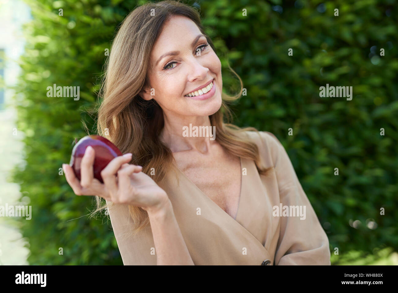 Ritratto di donna matura tenendo un apple, hedge in background Foto Stock