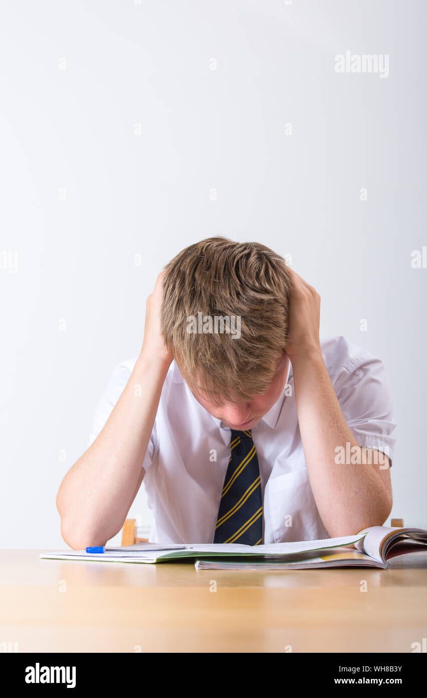 Un sottolineato scolaro con la testa tra le mani seduto alla sua scrivania Foto Stock