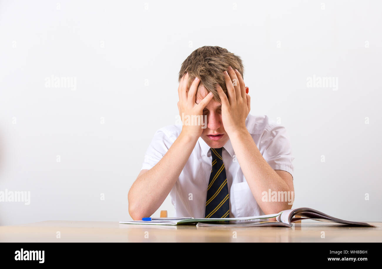 Un sottolineato scolaro con la testa tra le mani seduto alla sua scrivania Foto Stock