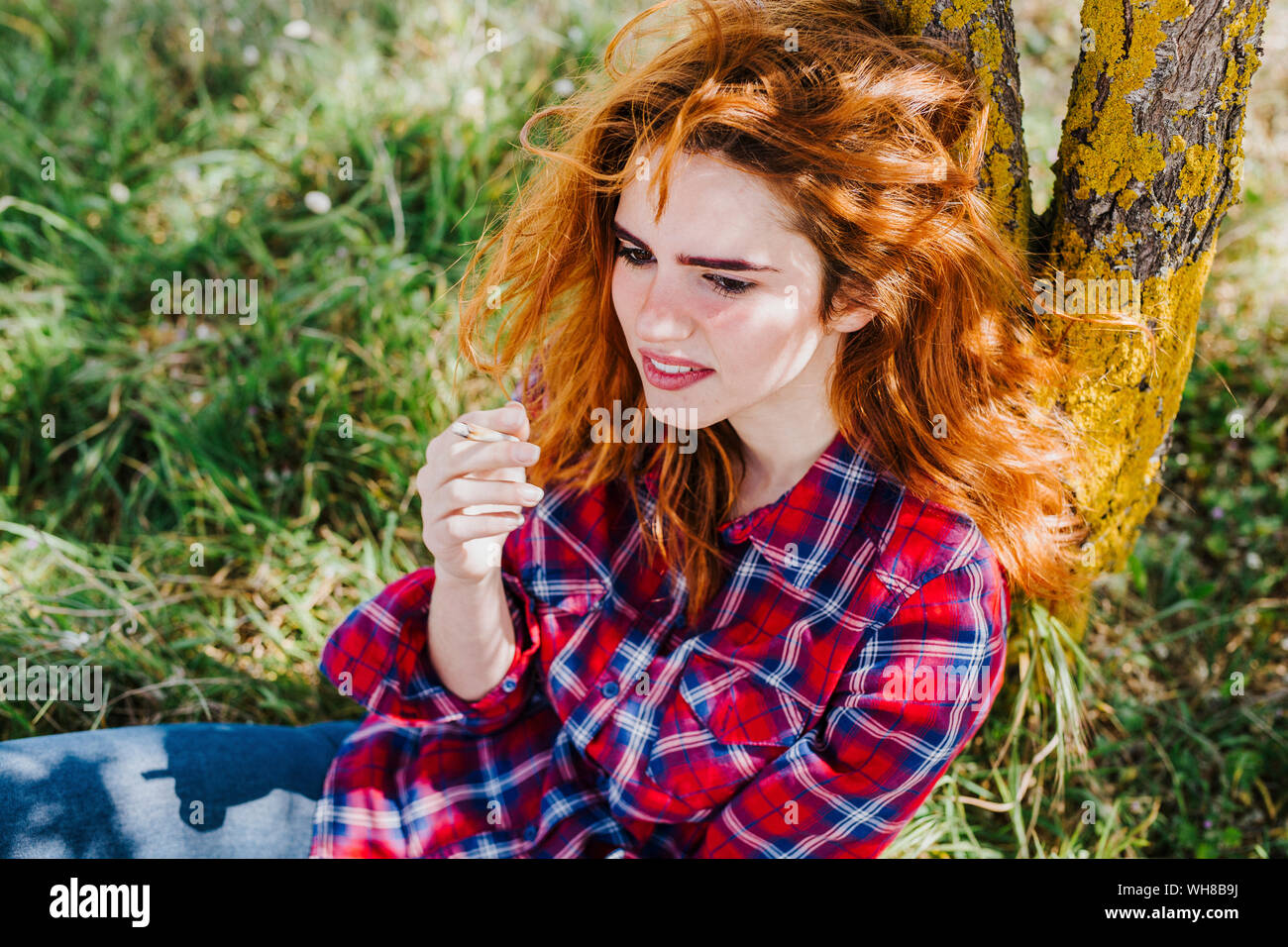 Ritratto di donna redheaded avente pausa sigaretta sotto un albero Foto Stock
