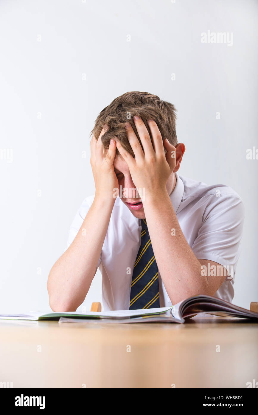 Un sottolineato scolaro con la testa tra le mani seduto alla sua scrivania Foto Stock