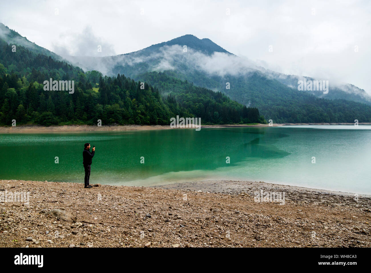 Uomo in piedi sul lungolago di scattare una foto con il suo smartphone, Wiestal serbatoio, Stato di Salisburgo, Austria Foto Stock