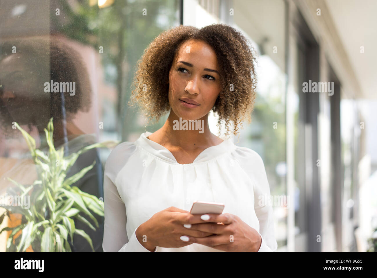 Ritratto di giovane donna con lo smartphone appoggiata contro la finestra di visualizzazione Foto Stock