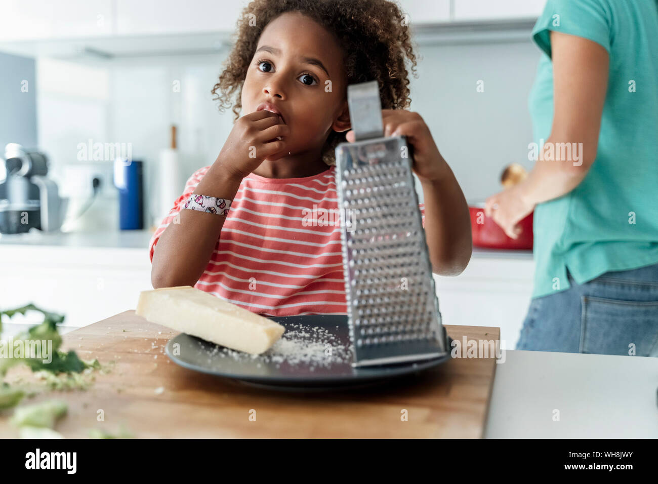 Ragazza la cottura con la madre in cucina degustazione di formaggio grattugiato Foto Stock