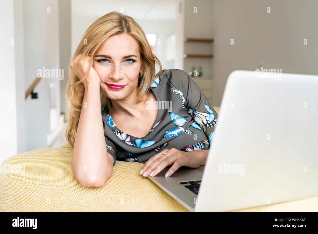 Ritratto di una giovane donna con il computer portatile sul lettino a casa Foto Stock