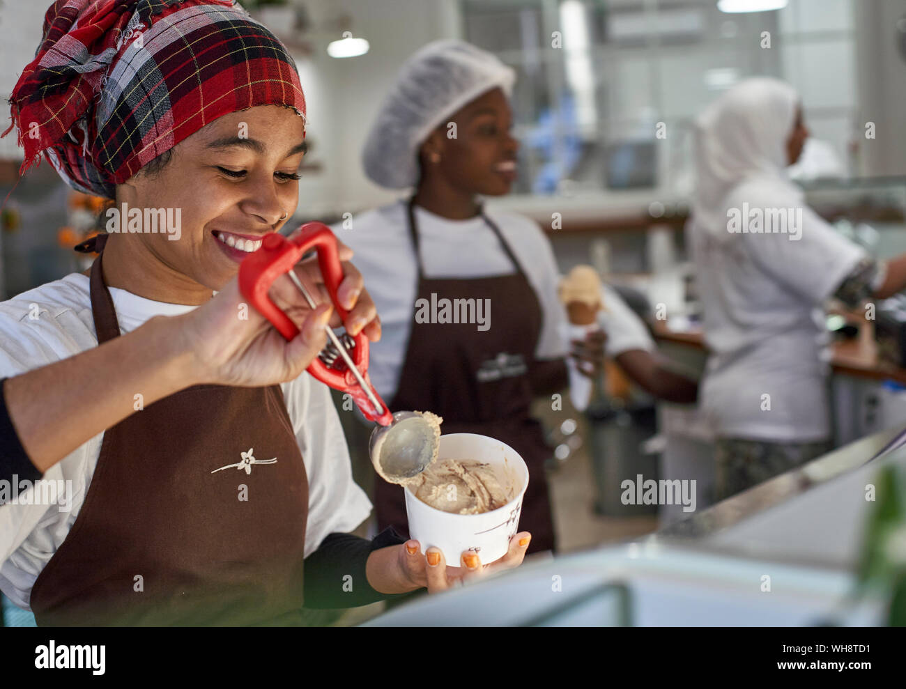 Giovane donna lavora in gelateria, misurino di riempimento con gelato Foto Stock