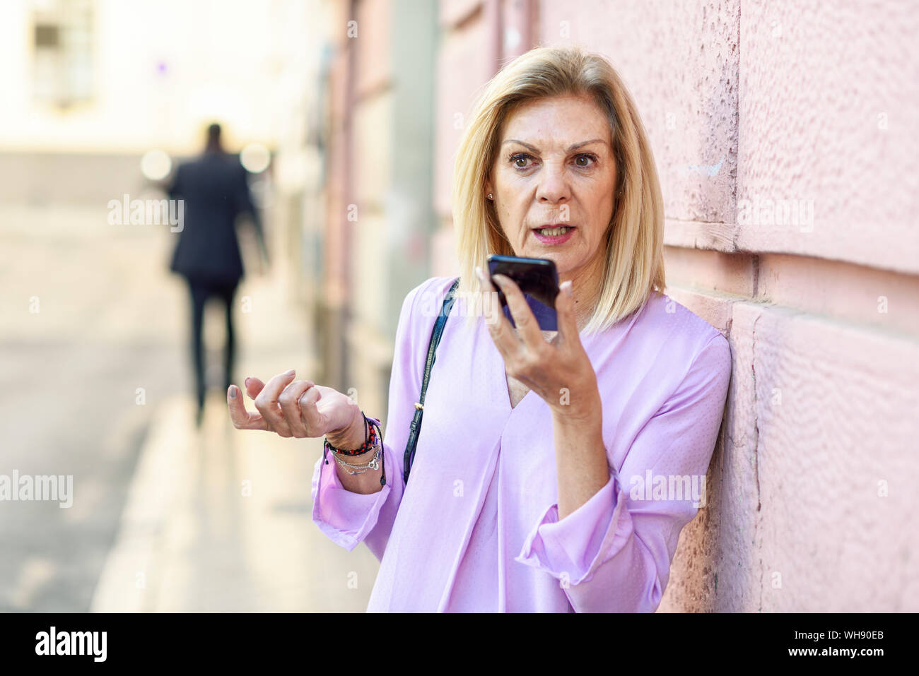 Donna matura utilizza lo smartphone nella città Foto Stock