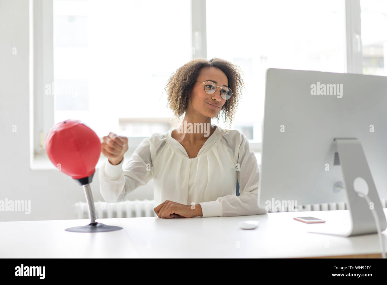 Ritratto di giovane freelancer seduto alla scrivania in ufficio boxing palla di punzonatura mentre guarda il computer Foto Stock