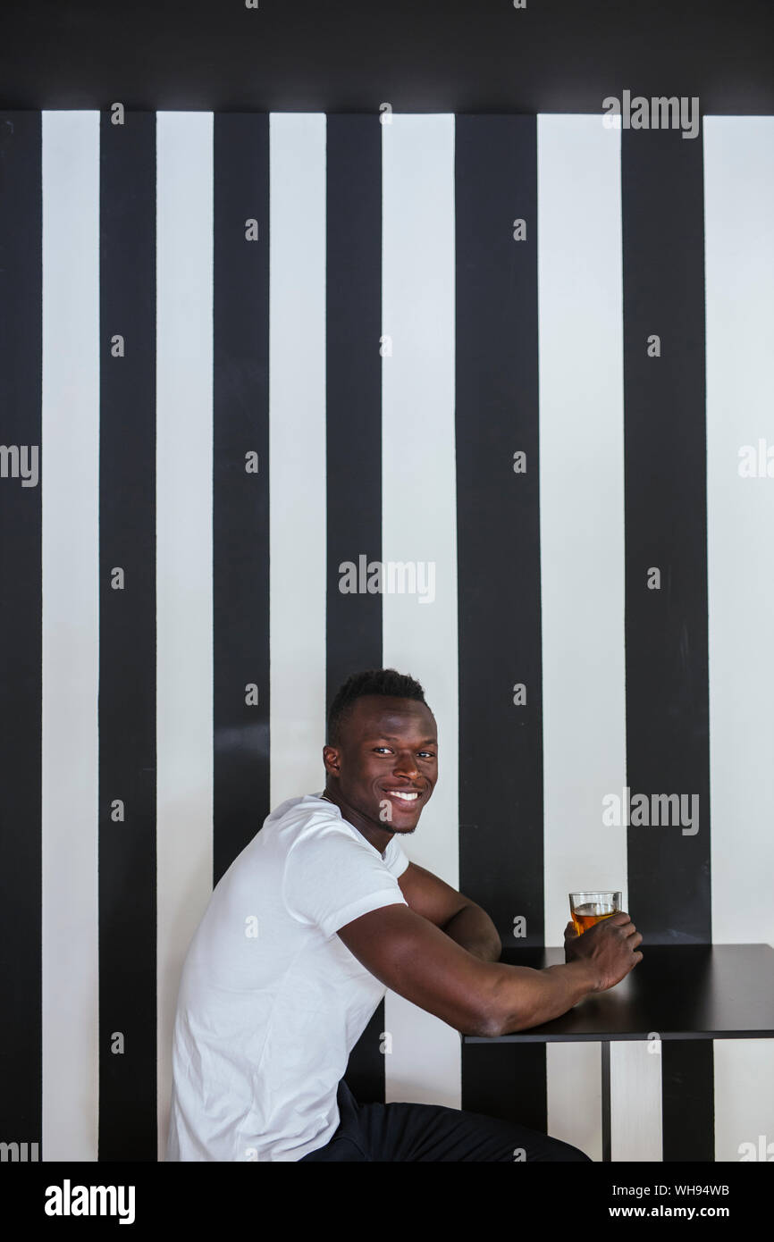 Ritratto di giovane sorridente uomo seduto a tavola con un drink Foto Stock