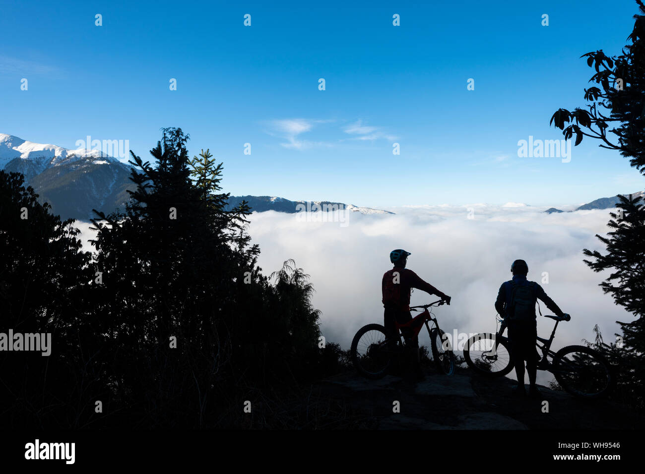 I ciclisti di montagna si affacciano su una valle riempita con una inversione di cloud in Himalaya durante la mountain bike nella regione Gosainkund, regione Langtang, Nepal Foto Stock