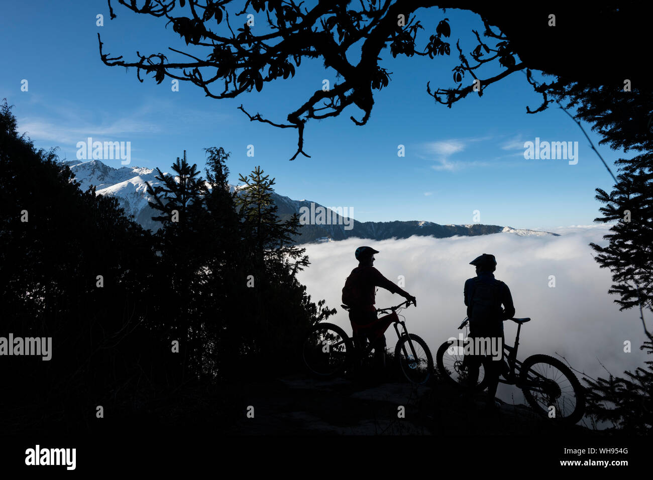 I ciclisti di montagna si affacciano su una valle riempita con una inversione di cloud in Himalaya durante la mountain bike nella regione Gosainkund, regione Langtang, Nepal Foto Stock
