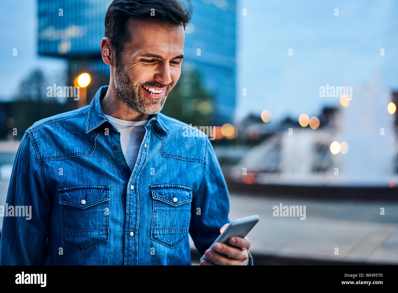 Ritratto di uomo utilizza lo smartphone mentre fuori in città durante la sera Foto Stock