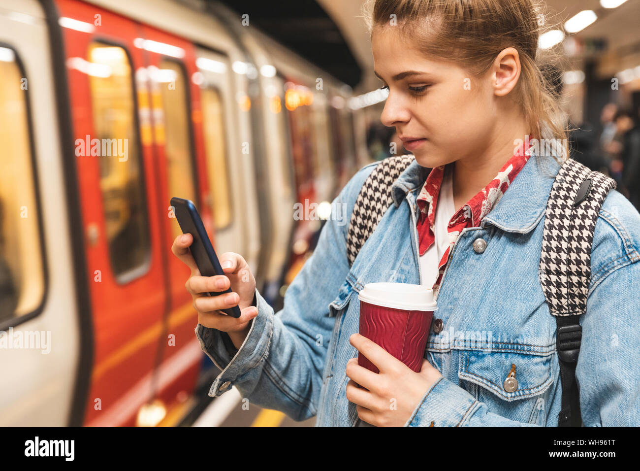 Giovane donna alla stazione della metropolitana utilizzando uno smartphone Foto Stock