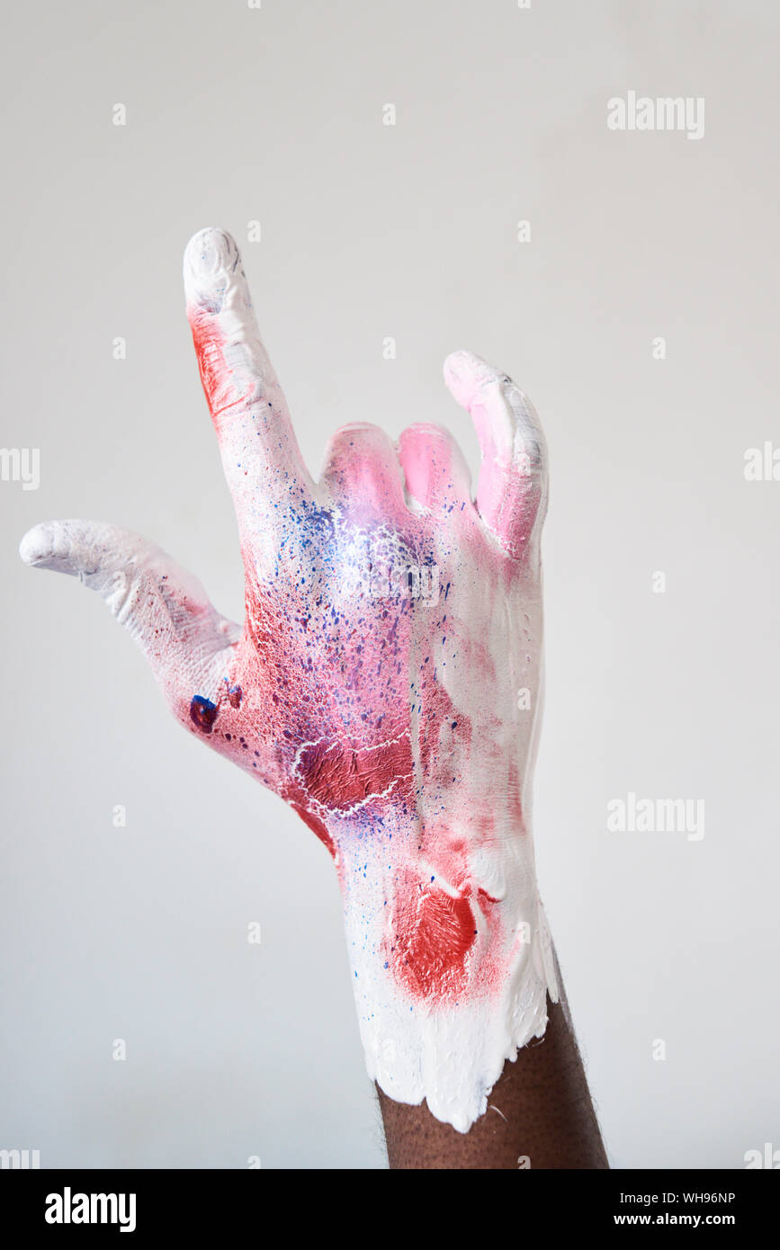 Artista mano ricoperto in vernice colorata mentre facendo il segno delle corna Foto Stock
