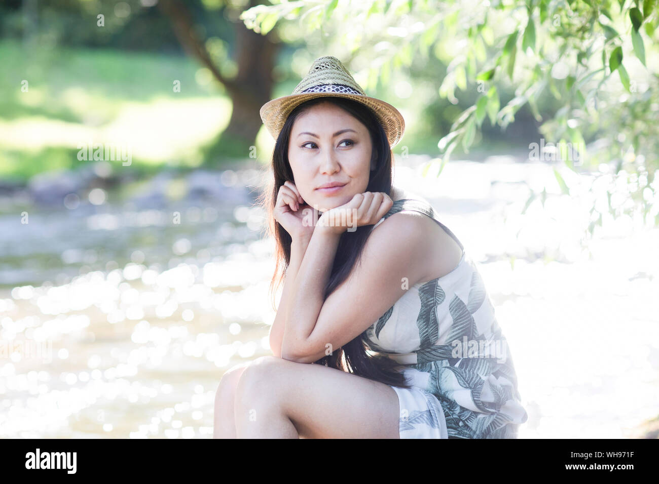 Giovane donna che indossa un cappello di paglia e seduti in riva al fiume Foto Stock