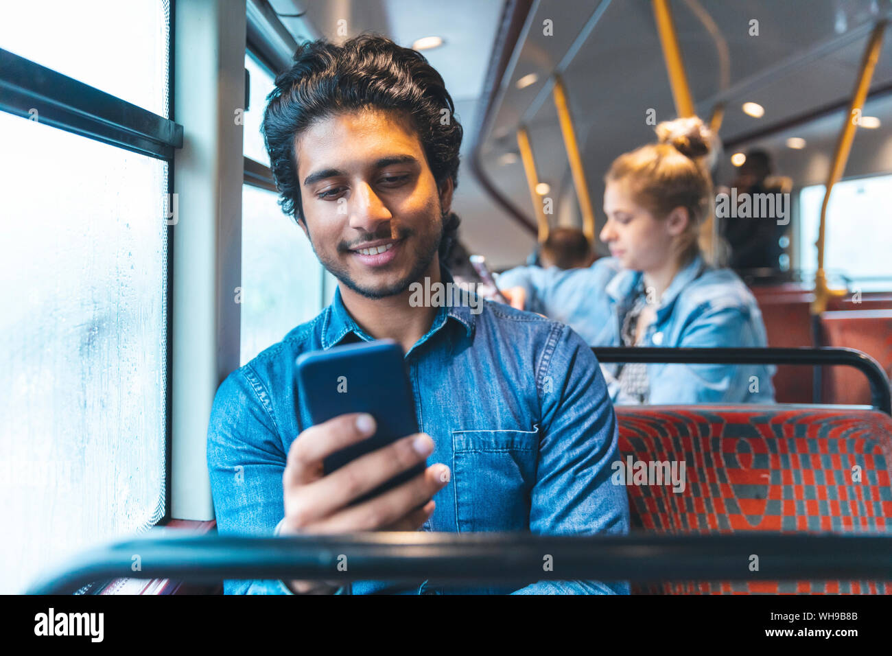 Ritratto di giovane uomo che viaggia in autobus guardando al telefono cellulare, London, Regno Unito Foto Stock