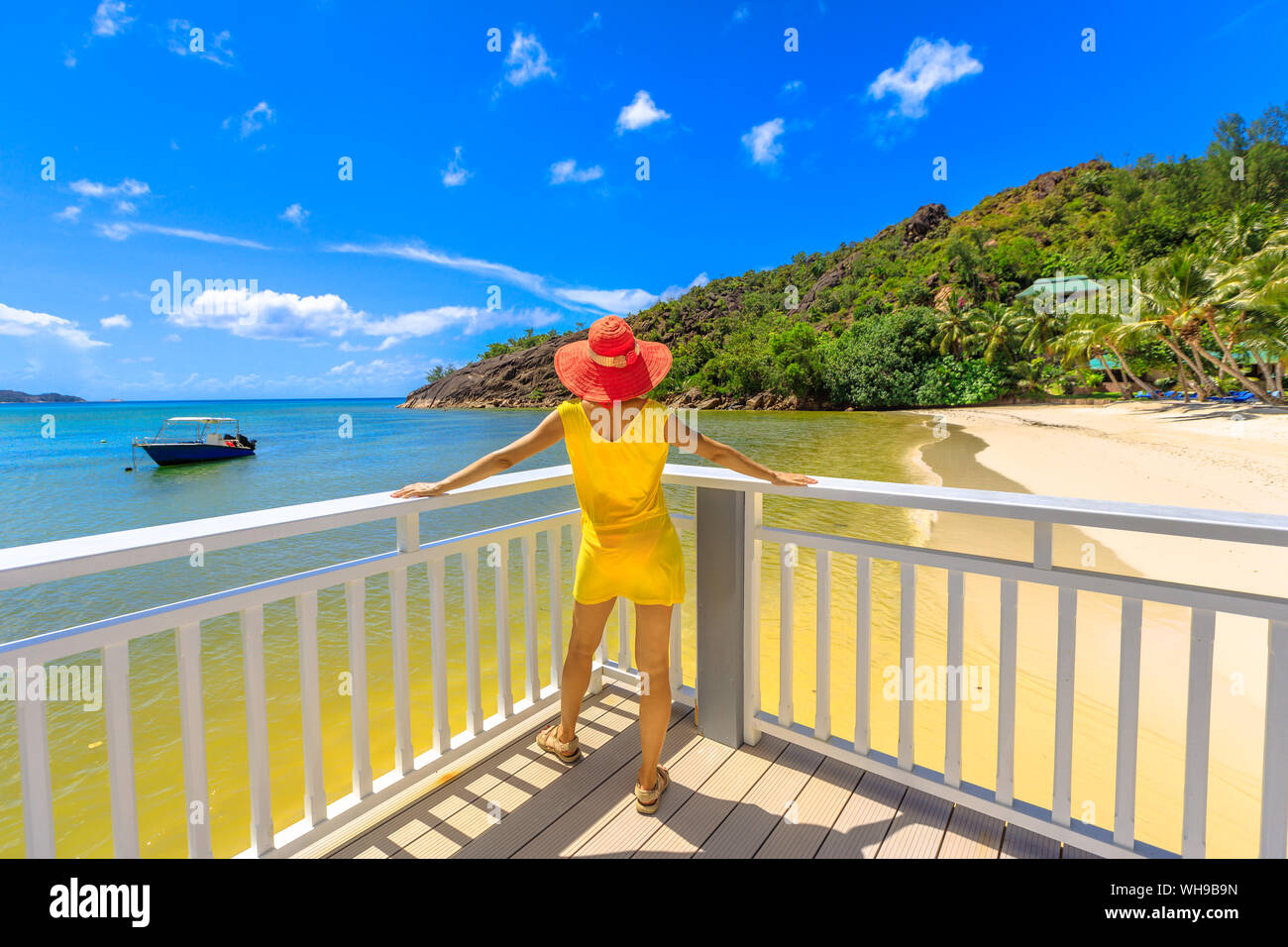 Donna in abito giallo sul balcone del pontile in legno, guardando all immacolata spiaggia bianca di Anse Gouvernement, vicino a Cote d'Or Bay, a Praslin, Seicelle Foto Stock