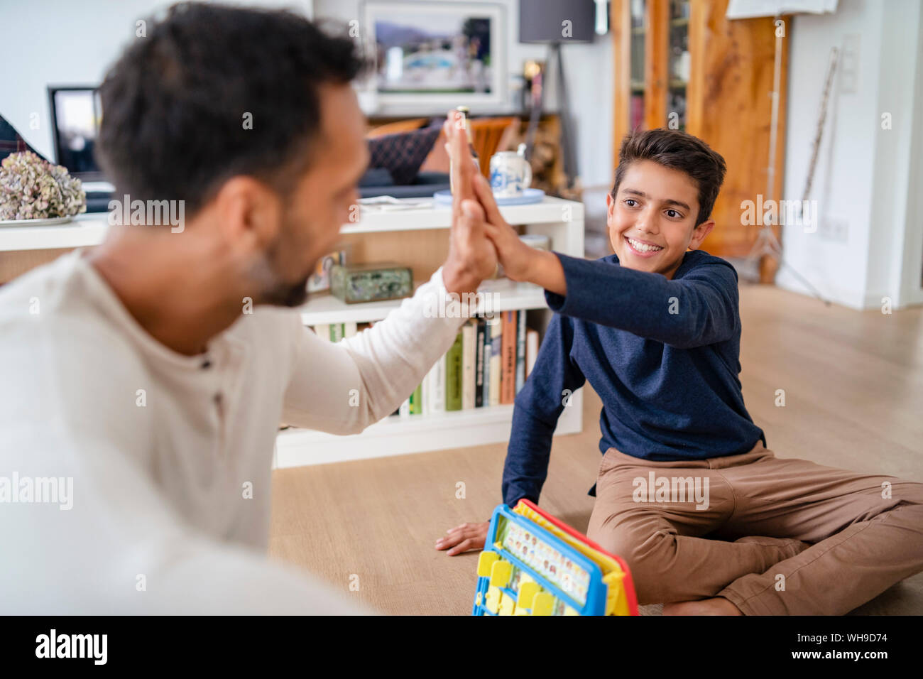 Padre e Figlio seduto sul pavimento a casa giocando a un gioco e alta fiving Foto Stock