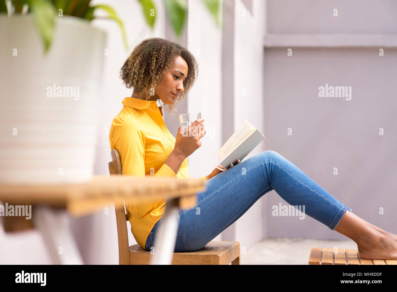 Giovane donna di rilassarsi con un bicchiere di acqua la lettura di un libro Foto Stock