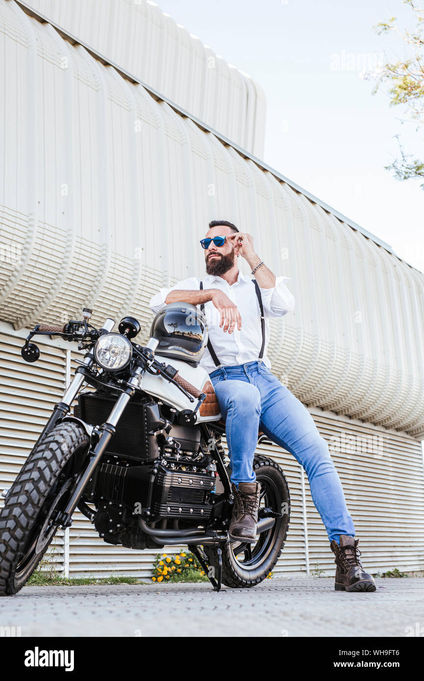 Ritratto di barbuto motociclista in mirroring con occhiali da sole appoggiata sulla sua moto Foto Stock