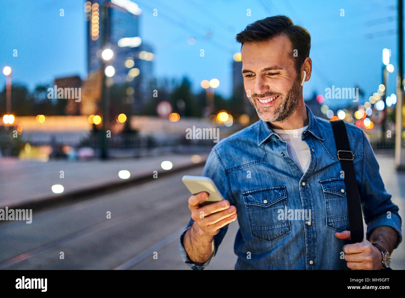 Uomo in piedi con lo smartphone in attesa per commutare la sera dopo il lavoro Foto Stock