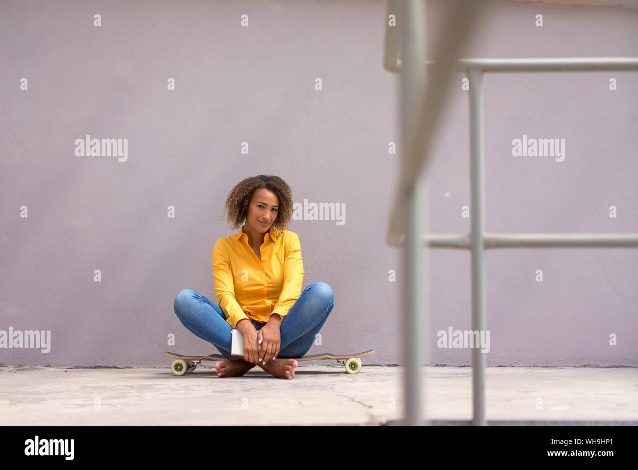 Ritratto di giovane donna libro seduti a piedi nudi su skateboard Foto Stock