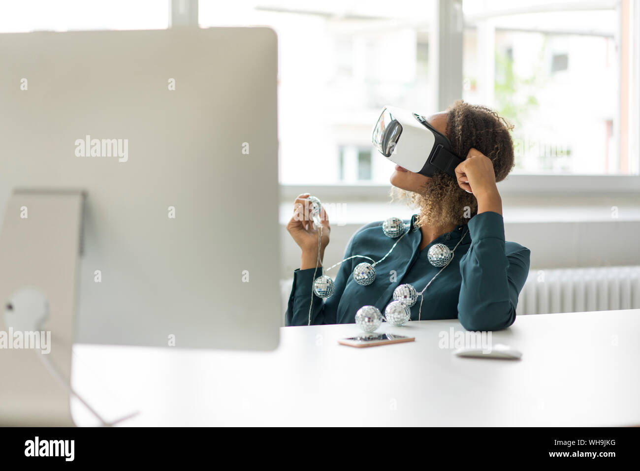 Giovane donna seduta alla scrivania con catena di luci utilizzando occhiali per realtà virtuale Foto Stock