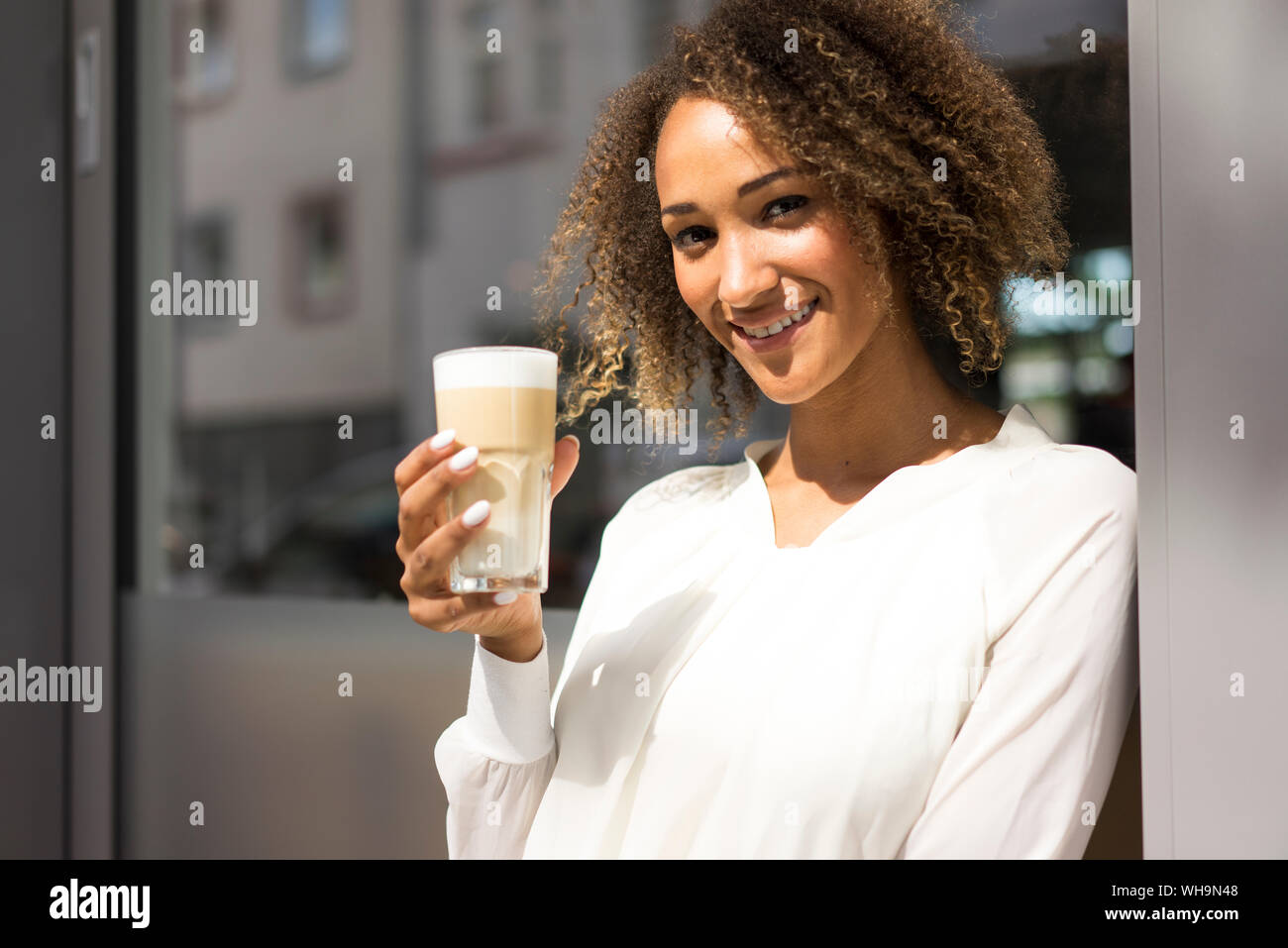 Ritratto di sorridente giovane donna in un momento di relax a pavement cafe con Latte Macchiato Foto Stock