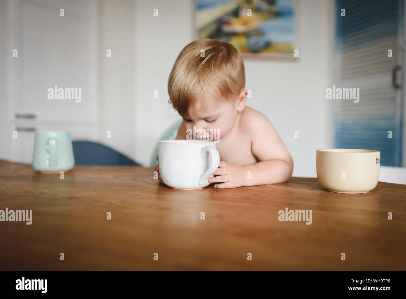 Shirtless piccolo ragazzo seduto al tavolo della cucina cercando in tazza Foto Stock