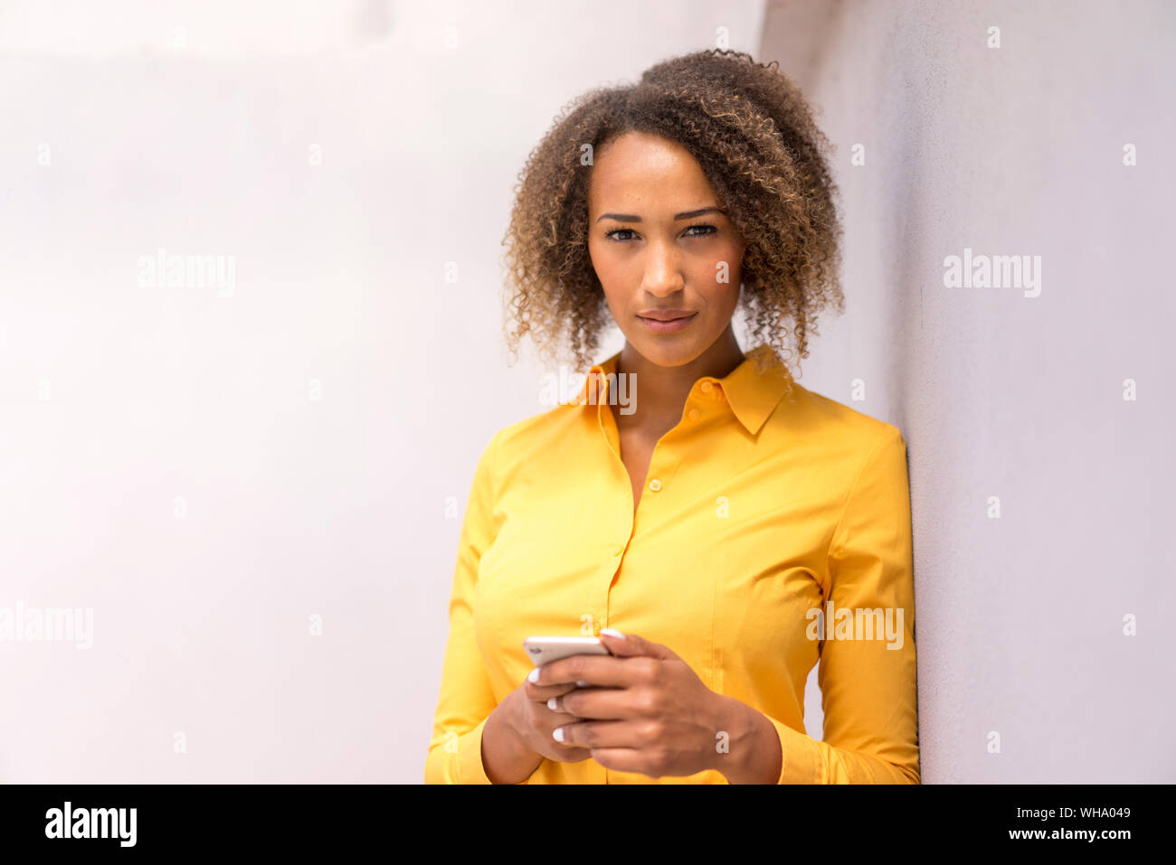 Ritratto di giovane donna con un telefono cellulare da indossare magliette di colore giallo Foto Stock