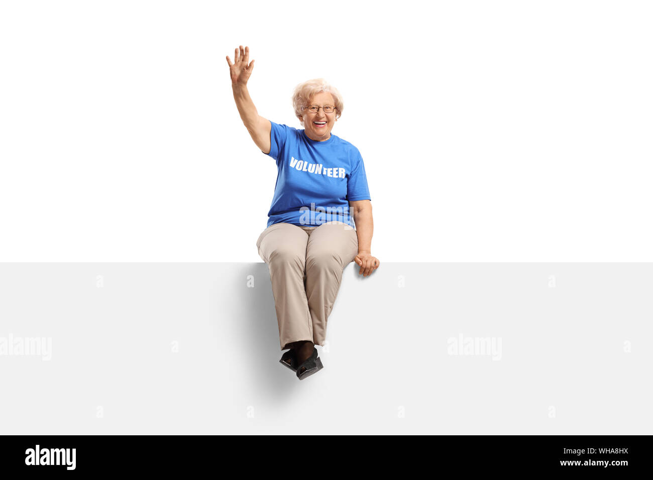 A piena lunghezza shot di una donna anziana volontario seduto su un pannello bianco e agitando isolati su sfondo bianco Foto Stock