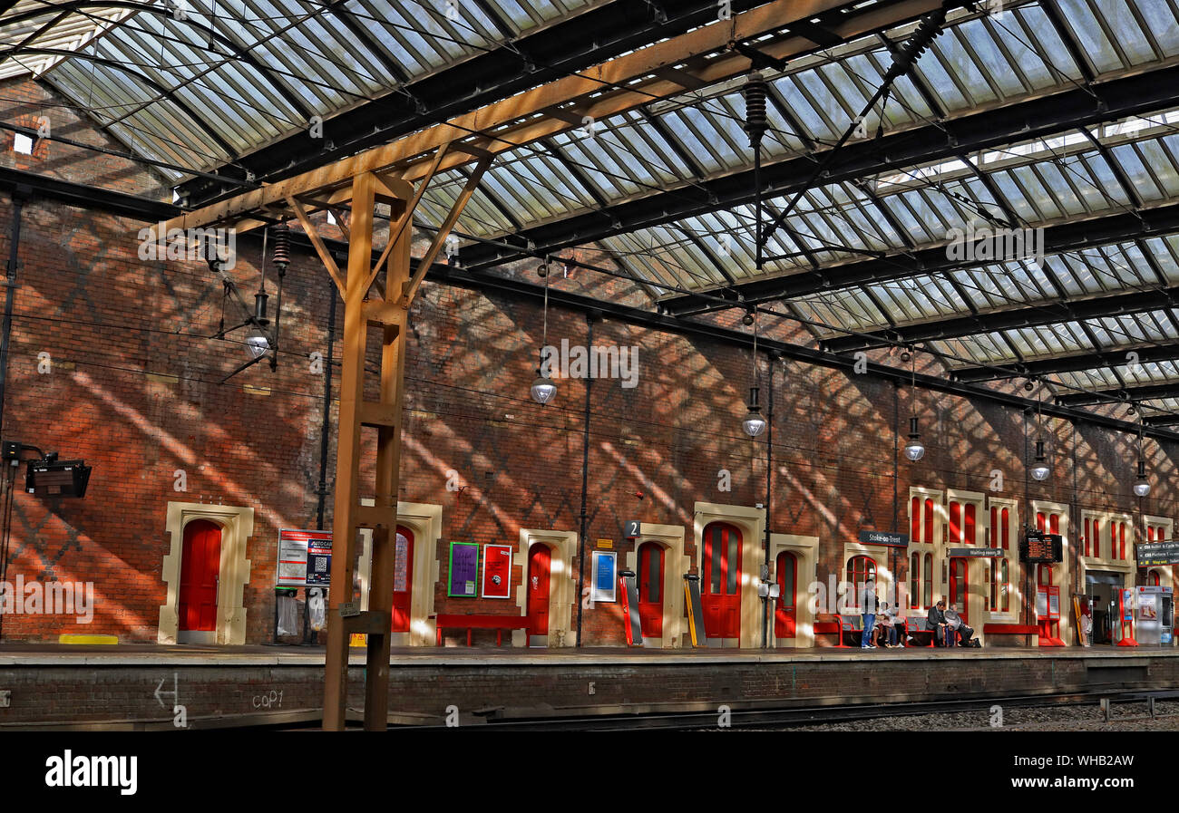 Forte sole estivo crea ombre attraverso il grande muro di mattoni e porte come passeggeri attendere un treno in direzione nord a Stoke on Trent ferrovia 23.8.19. Foto Stock